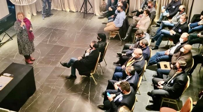 Na foto com ângulo de cima, Adeliana Dal Pont aparece a frente segurando um microfone falando para um grupo de pessoas sentadas em cadeiras. O evento do PSD oficializou a pré-candidatura de três nomes ao governo do estado em 2022.