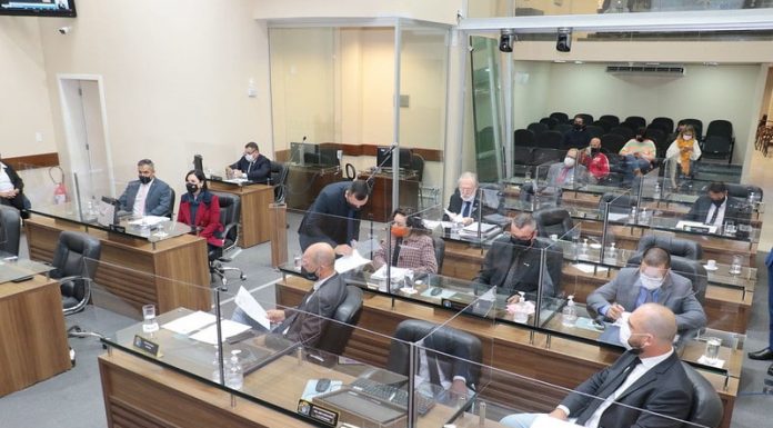 vereadores sentados nas bancadas da câmara de florianópolis separados por vidros, usando máscaras