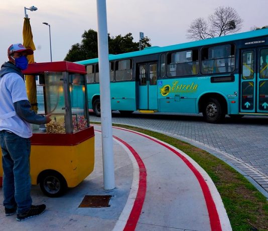 ônibus de transporte intermuicipal da empresa estrela saindo sda ponte herc´pilio luz e na calçada em primeiro plano pipoqueiro usando máscara com carrinho de pipoca