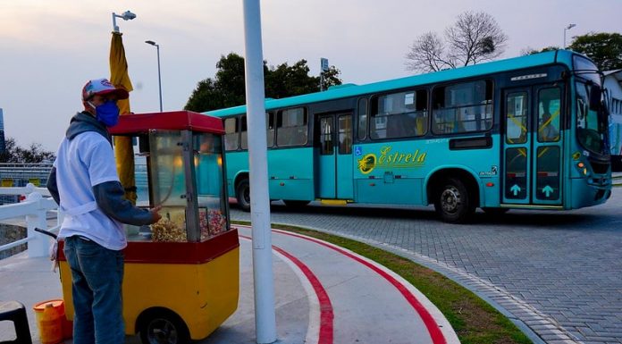 ônibus de transporte intermuicipal da empresa estrela saindo sda ponte herc´pilio luz e na calçada em primeiro plano pipoqueiro usando máscara com carrinho de pipoca