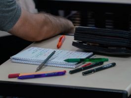 caderno, lápis e canetas em cima de mesa com homem ao lado