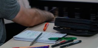 caderno, lápis e canetas em cima de mesa com homem ao lado