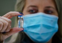 mulher usando máscara segura ampola de dose de vacina de covid