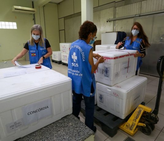 Governo distribui 125 mil doses que seriam de reforço para aplicação de 1ª dose Governo distribui 125 mil doses que seriam de reforço para aplicação de 1ª dose - mulheres da vigilância organizando caixas de isopor com as doses
