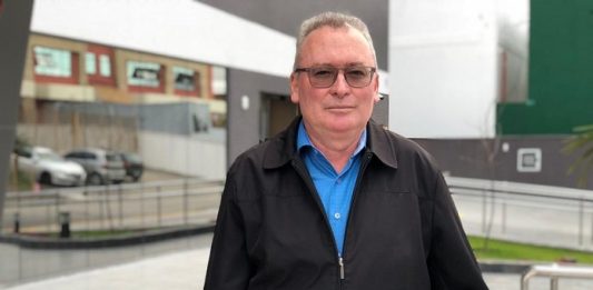 Mobilidade na Grande Florianópolis homem com jaqueta marrom e camisa azul, de pé escorado no corrimão