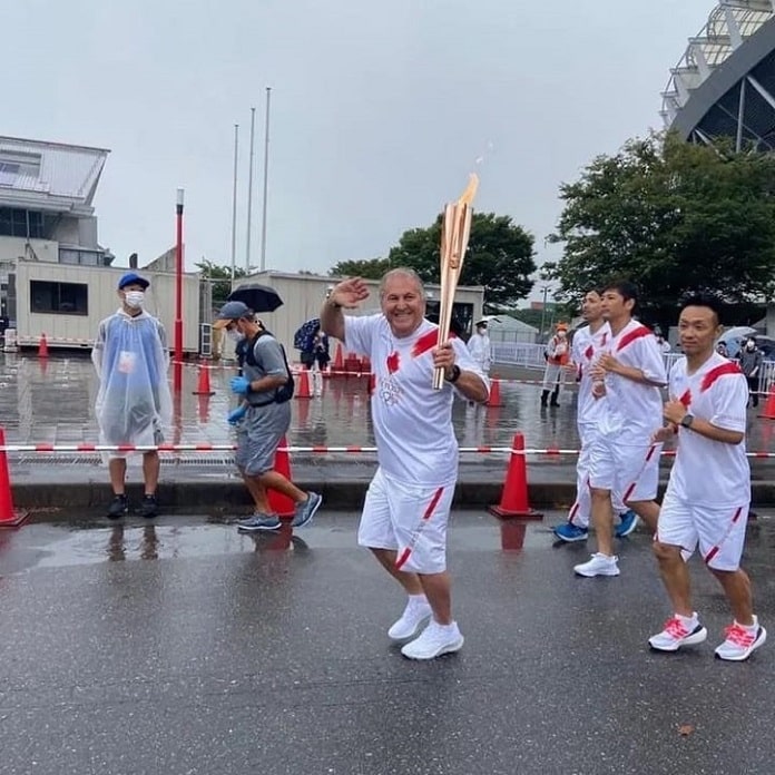 Zico vestindo camiseta e calção branco com listras vermelha, carregando a tocha olimpica