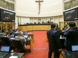 plenário da alesc, com uma cruz religiosa no alto e deputados em pé e sentados, as telas mostram a votação do pl que prevê notebooks para professores da rede pública estadual de Santa Catarina