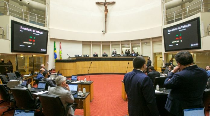 plenário da alesc, com uma cruz religiosa no alto e deputados em pé e sentados, as telas mostram a votação do pl que prevê notebooks para professores da rede pública estadual de Santa Catarina