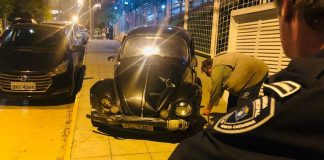 Parte de um guarda municipal aparece na foto de costas olhando para um fusca preto, que está ao centro da imagem em uma calçado. O veículo atropelou um motoboy em Florianópolis, no Itacorubi.