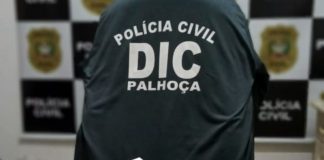 documento do inquérito com centenas de páginas sobre mesa com logo da dic e polícia civil ao fundo -