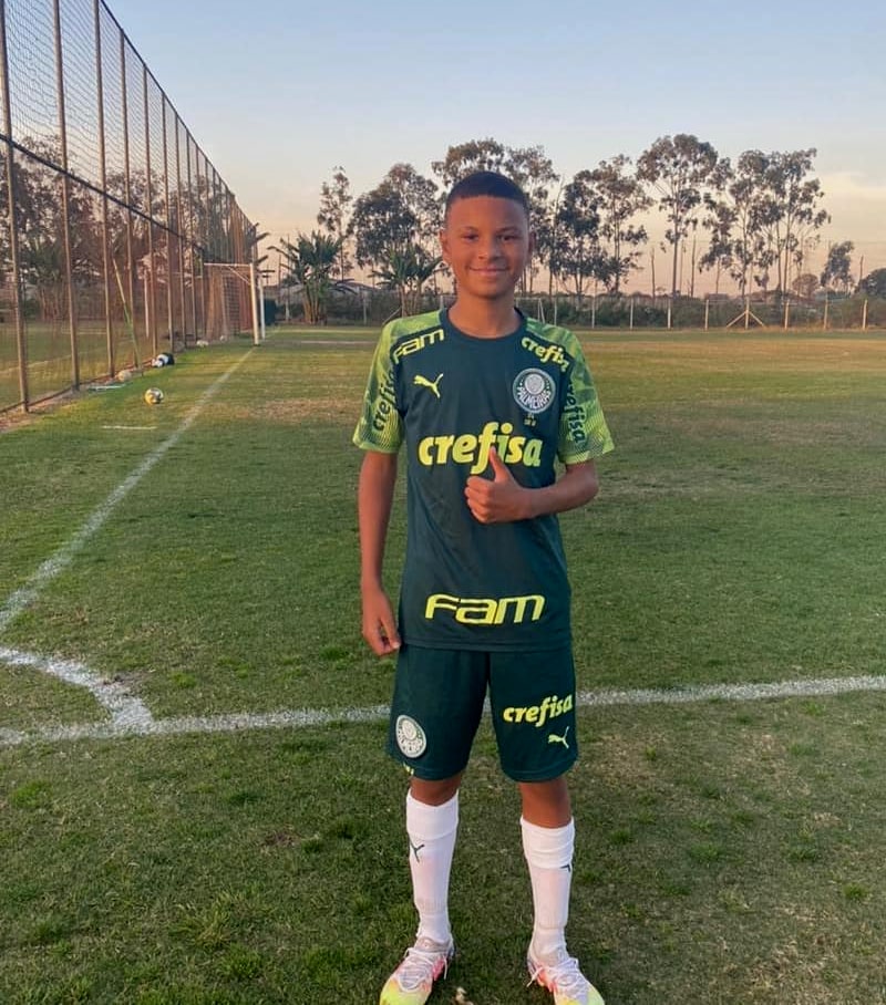 Gabriel da Cunha Santana posa para a foto usando uniforme do palmeiras na beira de campo de futebol