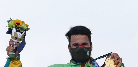 Ítalo Ferreira ganha 1º ouro do Brasil e do surfe nas Olimpíadas de Tóquio Ítalo Ferreira tem cabelos escuros e curtos, usa uma máscara preta e um agasalho verde e amarelo do Brasil, ele segura com a mão a medalha de ouro, conquistada no surfe, enroscada no pescoço e na outra mão levanta as flores entregues junto com a medalha nas olimpíadas de tóquio.