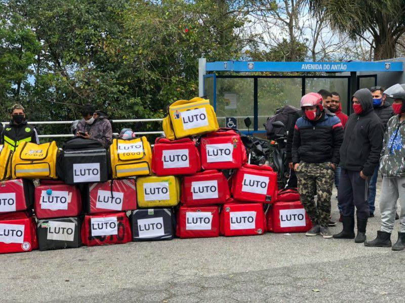 mochilas de entrega de motoqueiros empilhadas no chão todas com cartaz escrito "luto"