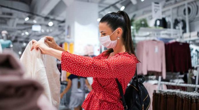 mulher usando máscara olha roupa em comércio - pagamento de 13º impulsiona economia de SC