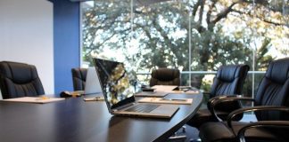 Uma mesa de escritório escura, com cadeiras em volta, um notebook em cima e uma janela ao fundo. A foto representa os novos negócios de Palhoça, que ficou em sexto lugar no ranking estadual.