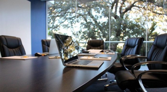 Uma mesa de escritório escura, com cadeiras em volta, um notebook em cima e uma janela ao fundo. A foto representa os novos negócios de Palhoça, que ficou em sexto lugar no ranking estadual.