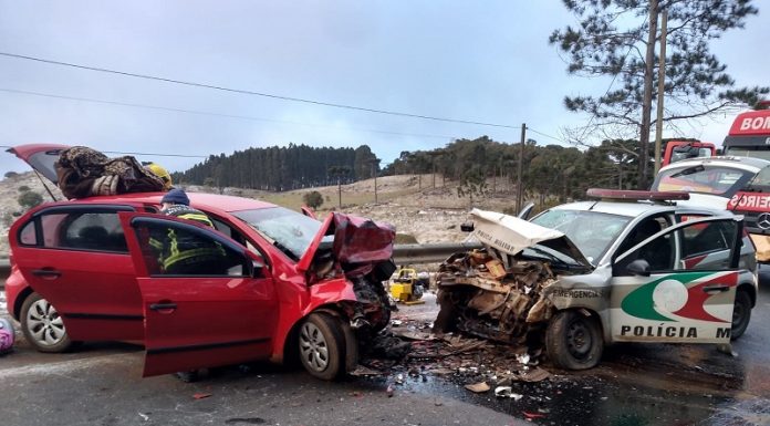 A foto mostra um veículo vermelho de frente para uma viatura da polícia militar, os dois veículos têm a parte da frente destruídas após uma colisão frontal, que deixou um policial morto e outros feridos em ANita Garibaldi. A pista tinha gelo no momento do acidente.
