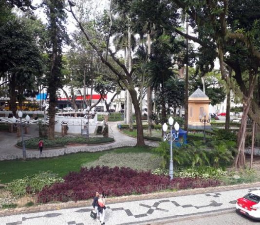 Praça XV em destaque com grandes árvores e calçadas; pessoas e taxi em primeiro plano - o local deve receber a Feira de Franklin Cascaes, evento cultural em Florianópolis