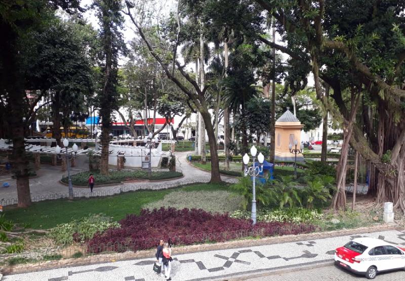 Praça XV em destaque com grandes árvores e calçadas; pessoas e taxi em primeiro plano - o local deve receber a Feira de Franklin Cascaes, evento cultural em Florianópolis