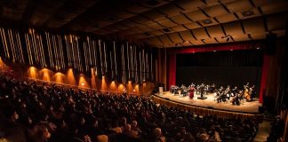 Primeiro evento-teste com público imunizado recebe cerca de 500 pessoas em SC - auditório lotado com orquestra cameratta no palco à frente