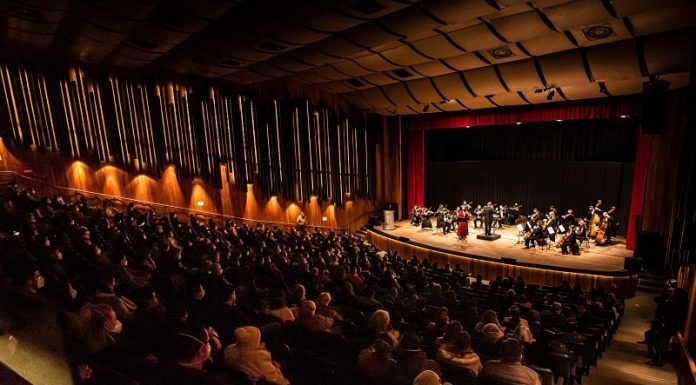 Primeiro evento-teste com público imunizado recebe cerca de 500 pessoas em SC - auditório lotado com orquestra cameratta no palco à frente