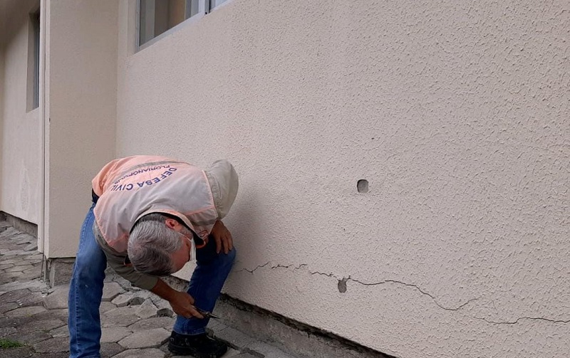 técnico da defesa civil de florianópolis se inclina para ver rachadura na parede da escola