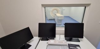 Em uma mesa branca, três telas pretas e ao fundo uma sala de tomografia. O hospital universitário da UFSC adquiriu um novo tomógrafo para exames, atendendo a população.