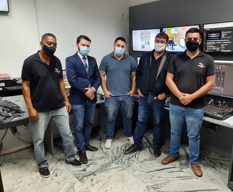 cinco homens usando máscara olham para a foto em pé dentro do estúdio da tv Câmara