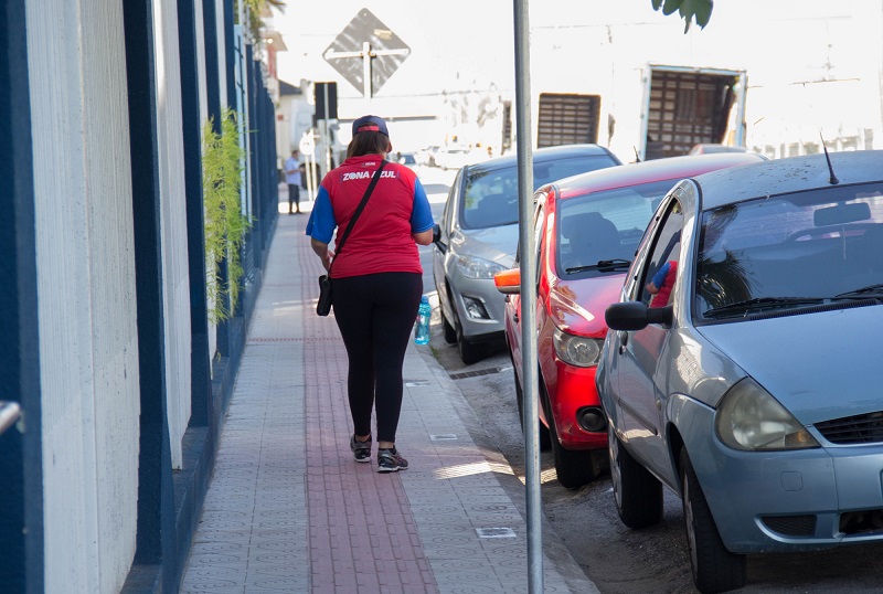fiscal da zona azul de são josé andando na calçada ao lado de carros estacionados