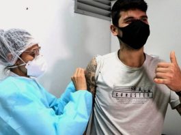7 em cada 10 adultos em Santa Catarina tomaram uma dose de vacina jovem recebe dose no braço fazendo sinal de positivo - 7 em cada 10 adultos em Santa Catarina já tomaram uma dose de vacina