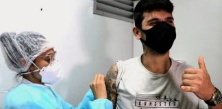 jovem recebe dose no braço fazendo sinal de positivo - 7 em cada 10 adultos em Santa Catarina já tomaram uma dose de vacina