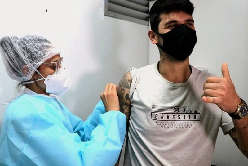 jovem recebe dose no braço fazendo sinal de positivo - 7 em cada 10 adultos em Santa Catarina já tomaram uma dose de vacina
