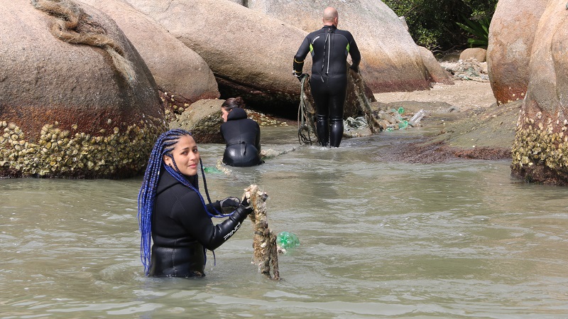 mulher sainda água com outros mergulhadores em bombinhas carregando lixo retirado do mar em bombinhas