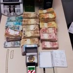 notas de dinheiro e outros objetos organizados sobre mesa - Polícia apreende R$ 347 mil do tráfico em kitnet em São José