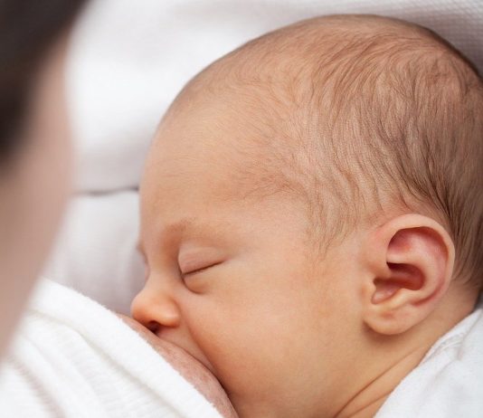 Um bebê aparece de olhos fechados mamando. A campanha Agosto Dourado promove a amamentação e a importância do aleitamento materno.