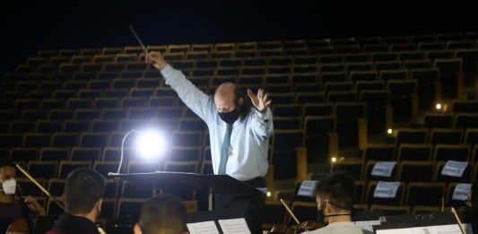 Concerto de retorno da Ossca terá plateia presencial, em São José maestro rege orquestra sinfônica de santa catarina e ao fundo auditório vazio