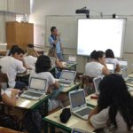 Uma sala de aula com um professor a frente olhando para um telão e observado por estudantes nas carteiras com computadores. O novo ensino médio em SC entra em vigor em 2022 nas escolas estaduais.