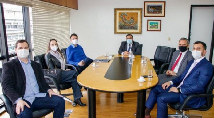 Seis pessoas sentadas ao redor de uma mesa amarela. Eles discutem ações de recuperação do dinheiro investido na compra dos respiradores em SC, iniciativa da PGE/SC.