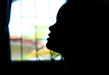 Uma janela ao fundo borrada na foto e o contorno de um rosto que aparece totalmente escuro pela foto. A prefeitura de Florianópolis criou o benefício desacolhimento, para mulheres vítimas de violência e jovens em casas de passagem.