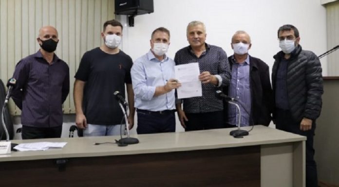 Seis homens usando máscara posam para a foto, dois do meio seguram um papel. Secretarias do estado e municipal de Palhoça estão promovendo a regularização fundiária de imóveis rurais, em Biguaçu e São João Batista, e urbanos em Palhoça.