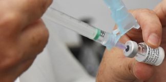 A imagem foca em um frasco de vacina com uma seringa, ambos segurados por uma mão branca. Nesta semana, o Ministério da saúde anunciou a aplicação da terceira dose da vacina contra covid-19 a partir de setembro.