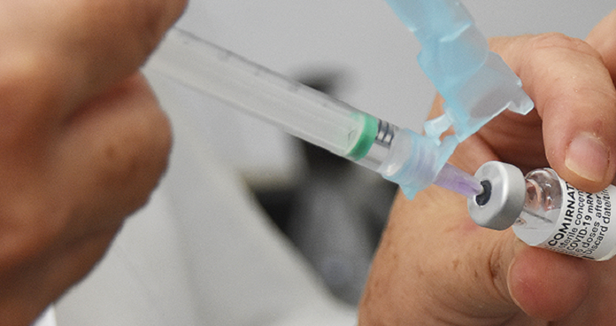 A imagem foca em um frasco de vacina com uma seringa, ambos segurados por uma mão branca. Nesta semana, o Ministério da saúde anunciou a aplicação da terceira dose da vacina contra covid-19 a partir de setembro.