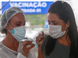mulher usando máscara recebe dose no braço - Vacinação em SC: Estado atinge 80% da população adulta vacinada com a primeira dose contra a Covid-19