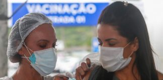 mulher usando máscara recebe dose no braço - Vacinação em SC: Estado atinge 80% da população adulta vacinada com a primeira dose contra a Covid-19