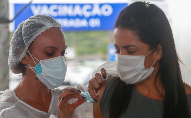 mulher usando máscara recebe dose no braço - Vacinação em SC: Estado atinge 80% da população adulta vacinada com a primeira dose contra a Covid-19