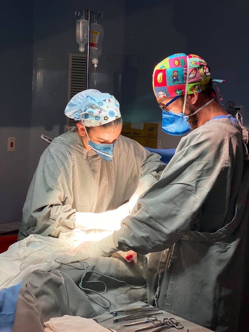 cirurgiã e cirugião em procedimento de cirurgia com foco de luz apenas no paciente, instrumentos em volta