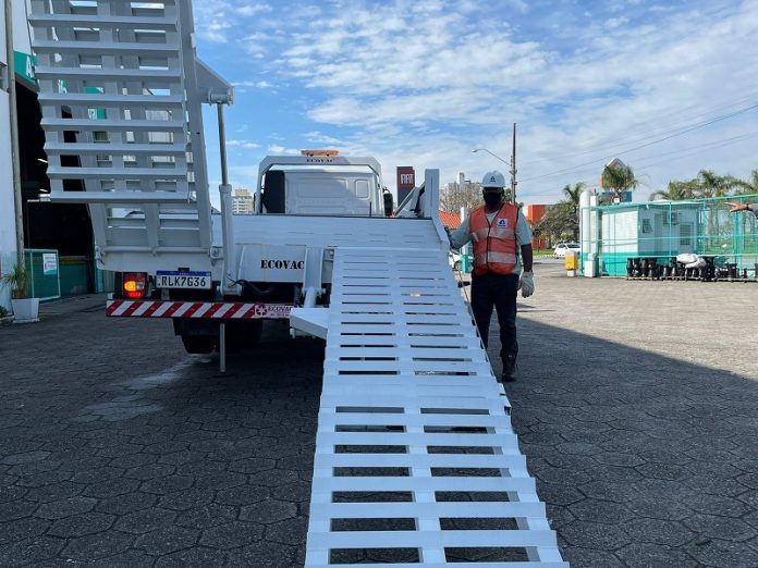 Um caminhão branco aparece de trás, com uma escada estendida e outra recolhida, há um funcionário de colete laranja ao lado. A foto ilustra a notícia de que a casan entregou um lote de equipamentos pesados em quatro superintendências.