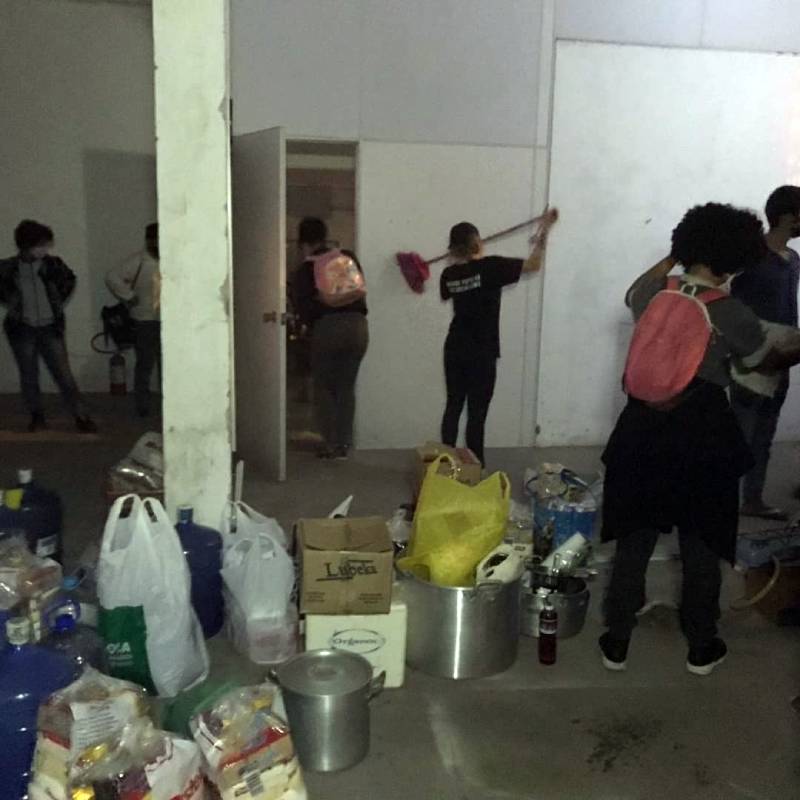 pessoas organizando espaço da ocupação onde há sacolas e outros objetos no chão