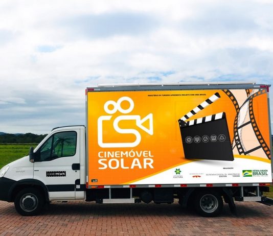 Foto se um caminhão de parte branca na frente e na parte de trás a cor laranja e o desenho de uma claquete de cinema e uma câmera, que identifica o veículo como cinemóvel solar, que chega em Palhoça na próxima semana para a exibição de dois filmes.