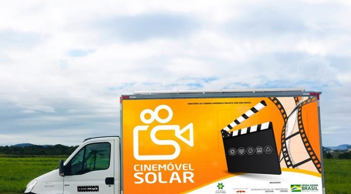 Foto se um caminhão de parte branca na frente e na parte de trás a cor laranja e o desenho de uma claquete de cinema e uma câmera, que identifica o veículo como cinemóvel solar, que chega em Palhoça na próxima semana para a exibição de dois filmes.